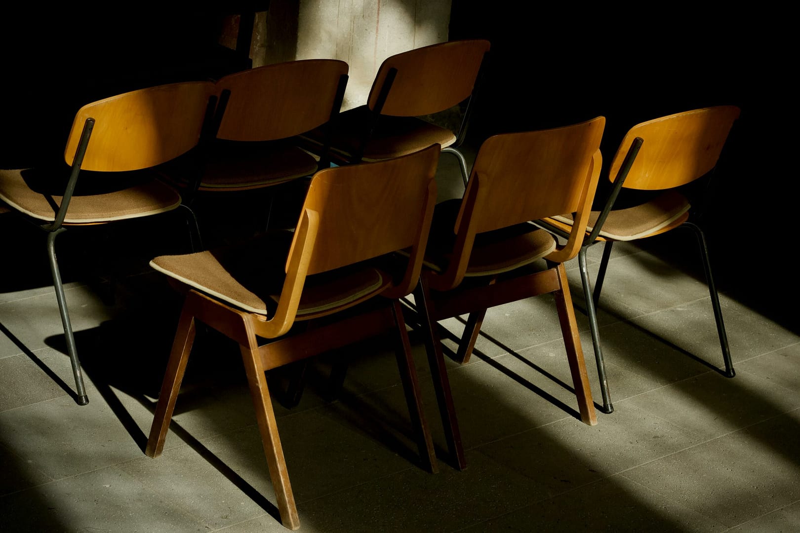A group of vintage wooden chairs artistically lit by soft, shadowy light.